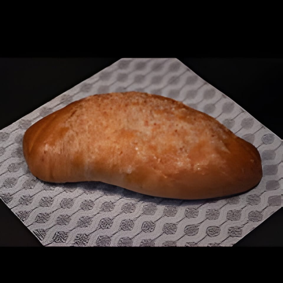 A golden-brown Colombian pan de bono, a type of cheese bread, rests on a patterned napkin.