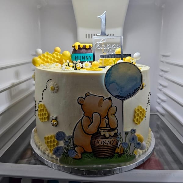 Winnie the Pooh themed birthday cake with honeycombs, bees, and a "Happy Birthday 1" topper.