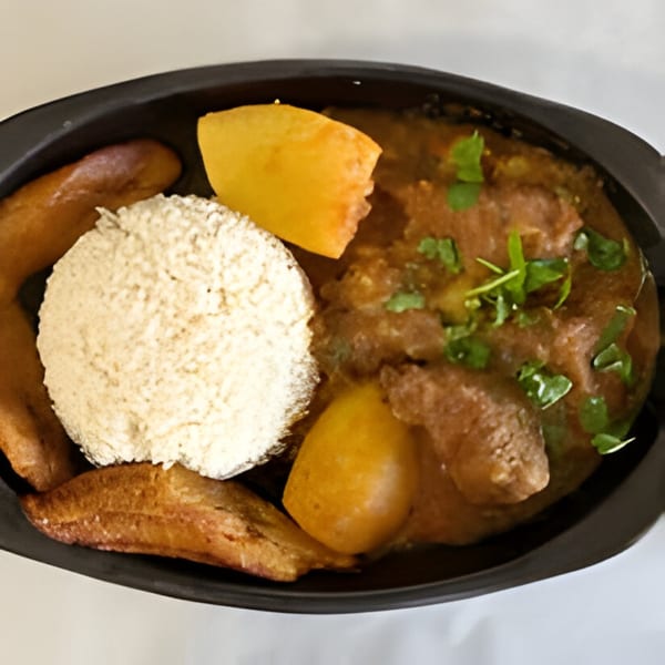 Colombian dish with stewed meat, potatoes, rice, and fried plantains in a black bowl.