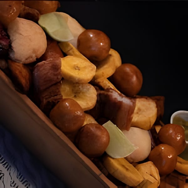 Close-up of a Colombian platter with fried plantains, buñuelos, and chicharrones, garnished with lime.