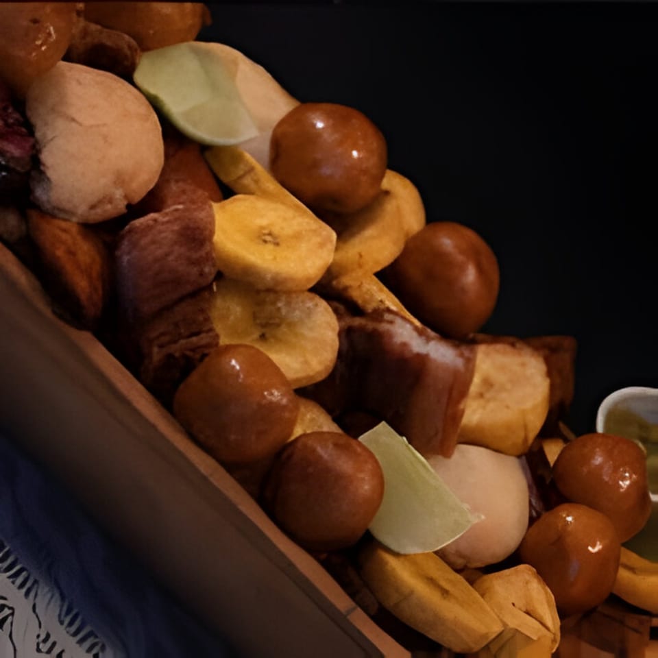 Close-up of a Colombian platter with fried plantains, buñuelos, and chicharrones, garnished with lime.