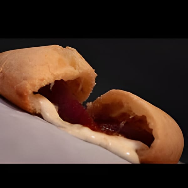 A Colombian guava and cheese pastry, known as a 'pastel de guayaba y queso', split open with filling oozing out.