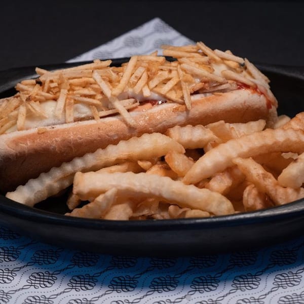 A Colombian hot dog topped with crispy potato sticks and a side of crinkle-cut fries.