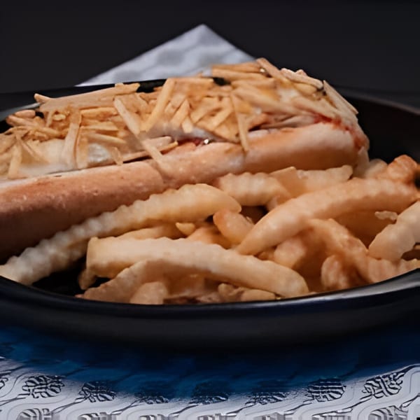 A Colombian hot dog topped with crispy potato sticks, served with a side of crinkle-cut fries.