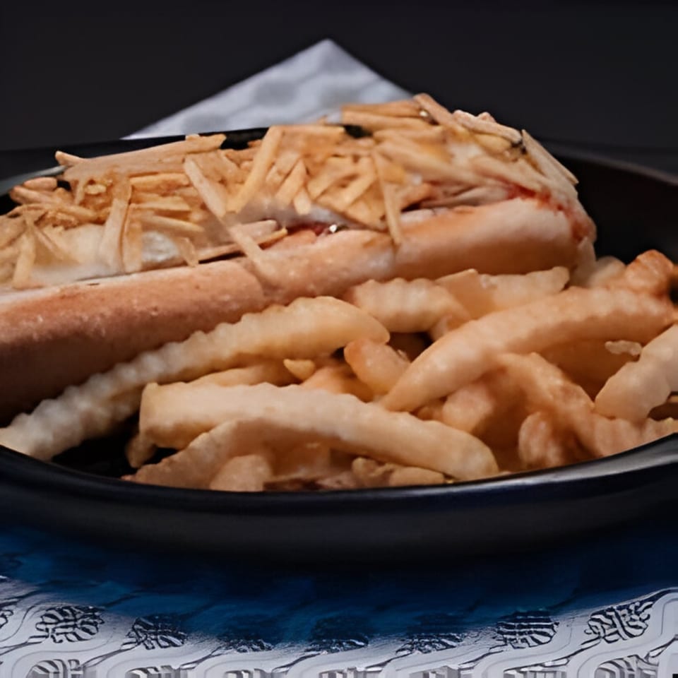 A Colombian hot dog topped with crispy potato sticks, served with a side of crinkle-cut fries.
