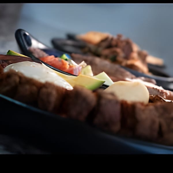 Close-up of Colombian food with meat, avocado, tomato, and white cheese on a black plate.