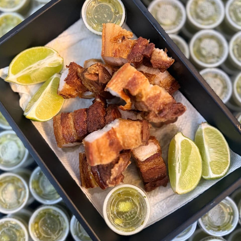 Crispy Colombian chicharrones with lime wedges and green sauce in a black tray.