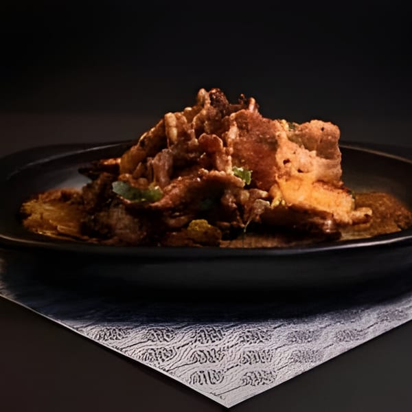A dark plate holds a pile of crispy, golden-brown Colombian chicharrones with green herbs.