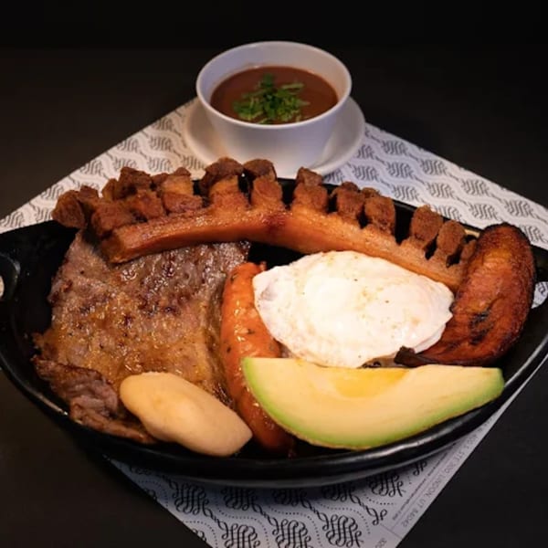 A Colombian bandeja paisa with steak, fried egg, chorizo, chicharron, avocado, and a side of beans.